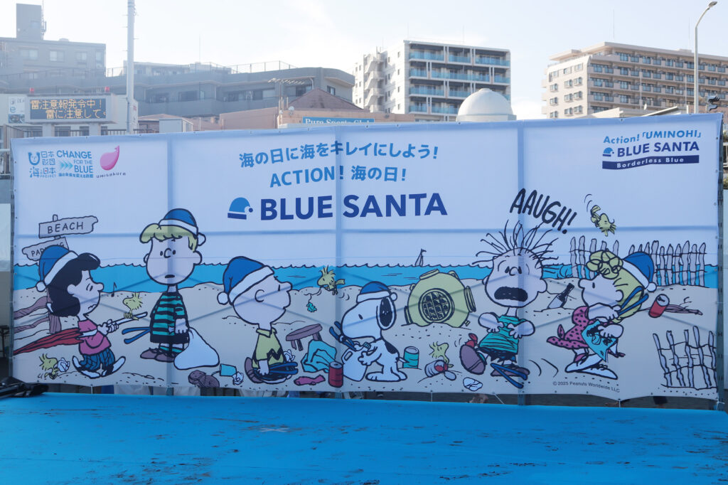 ごみ拾いイベントの受付エリアに設置された「BLUE SANTA 2025」スヌーピーデザインの立て看板