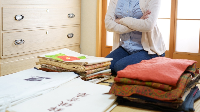 アパートの片付けが難しい理由を解説するセクションで使用する、荷物の前で腕を組み悩んでいる女性の様子が分かる写真