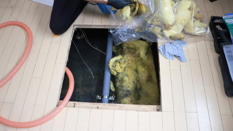 自社スタッフが撮影した床下浸水現場。床点検口から水濡れで劣化したグラスウール断熱材を取り出して袋に収納している実際の作業写真
