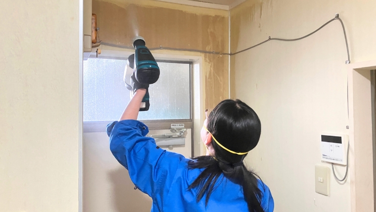 青い作業服とマスクを着用した自社スタッフが、電動工具を使って汚損した壁面・天井部を実際に処理している様子