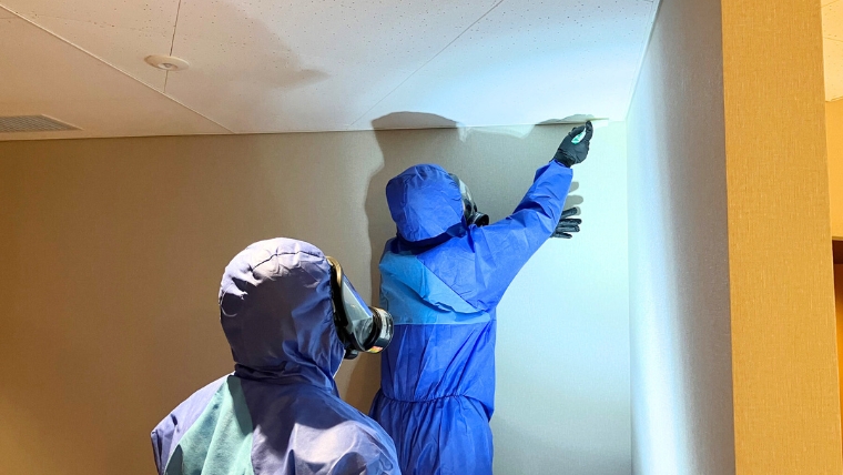 青い防護服と防毒マスクを着用した自社スタッフ2名が、賃貸物件の壁面カビを実際に除去・処理している様子