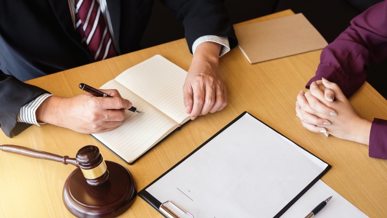 弁護士と思われる人物と依頼者が机を挟んで書類を確認している様子。法槌が置かれており、孤独死後の法的手続きに関するイメージ