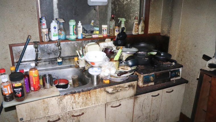 食器や調理器具が散乱し、壁や収納が黒く汚損したキッチンの様子