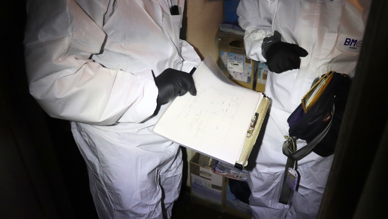 白い防護服と黒いグローブを着用した2名のスタッフがクリップボードの書類を確認している様子