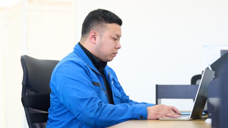 青い作業服を着用した自社スタッフがオフィスでノートパソコンに向かって対応している様子。特殊清掃の相談・見積もり対応のイメージ