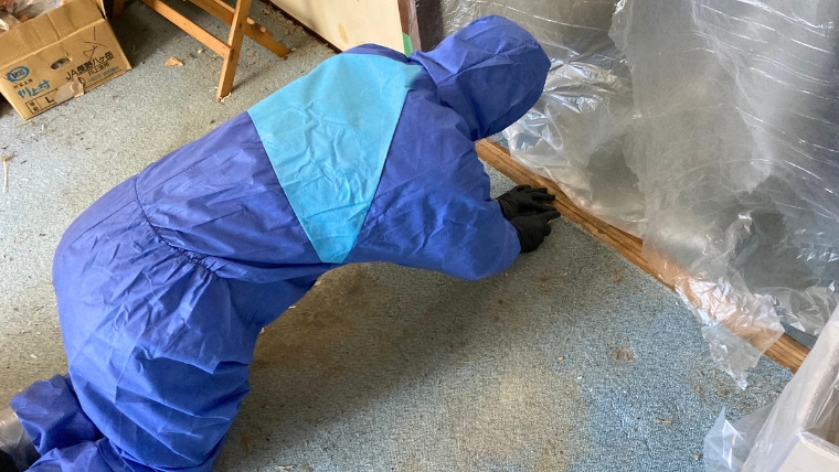 青い防護服と黒いゴム手袋を着用した自社スタッフが、特殊清掃現場でビニールシートを使ったゾーニング作業を実際に行っている様子
