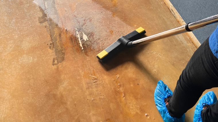 シューズカバーを着用した自社スタッフが、犬を飼っていた部屋のおしっこで変色・汚損したフローリングをバキューマーで実際に洗浄している様子