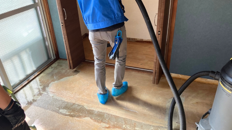 青いジャンパーとシューズカバーを着用した自社スタッフが、業務用湿式掃除機を使って汚損した床面を実際に洗浄している様子