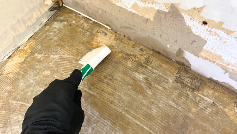 黒いゴム手袋を着用した自社スタッフが、汚損した床材をスクレーパーで実際に剥離・除去している様子