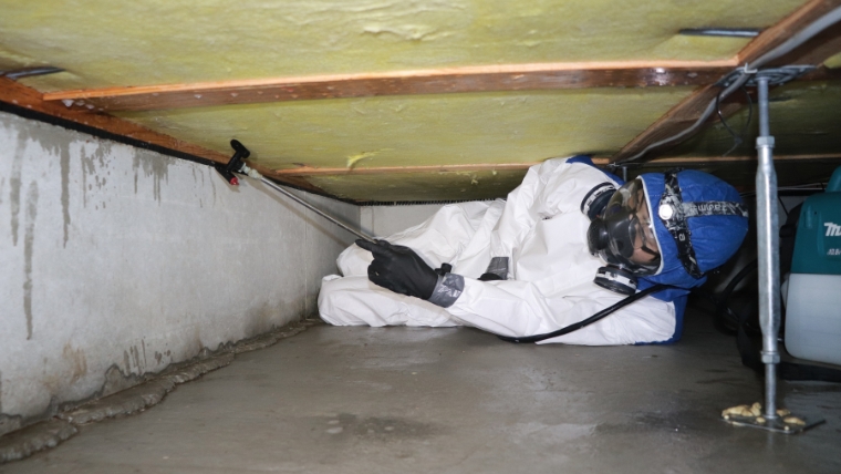 床下浸水後にPPEを装着した作業員が、床下空間の消毒作業を行っている様子