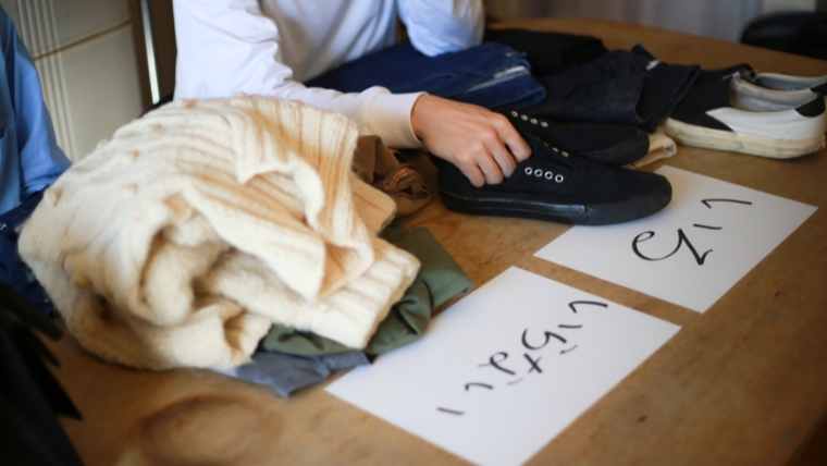 机の上に衣類・靴が並べられ「いる」「いらない」と書かれた仕分けラベルが置かれているイメージ。実家の片付けで買取サービスを活用し費用を抑える状況を想起させる