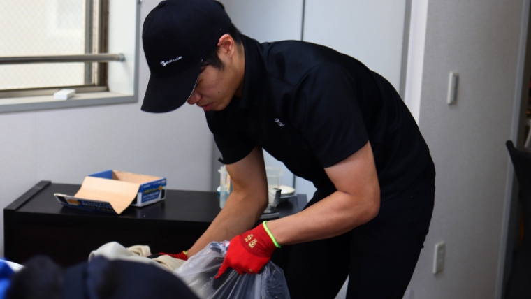 BLUECLEANロゴ入りキャップと赤いゴム手袋を着用したブルークリーンスタッフが、片付け現場で荷物の仕分け作業を実際に行っている様子