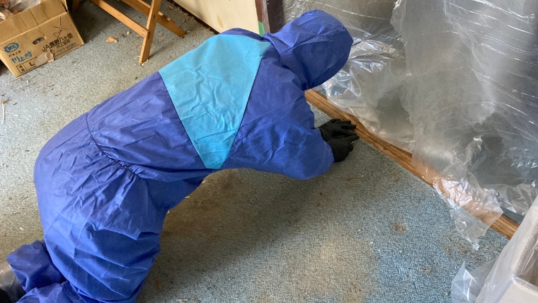 青い防護服と黒いゴム手袋を着用した自社スタッフが、孤独死現場でビニールシートを使ったゾーニング作業を実際に行っている様子