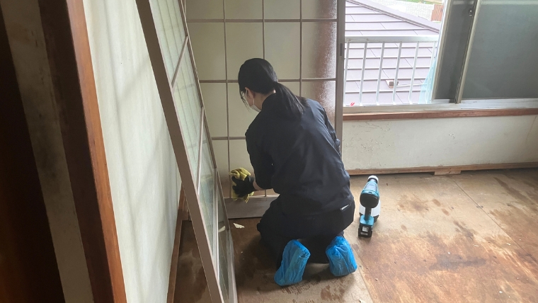 マスク・黄色いゴム手袋・シューズカバーを着用した自社女性スタッフが、和室の窓際でmakita製電動工具を傍らに床の清掃作業を実際に行っている様子