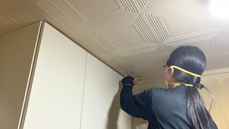 黒い手袋とゴーグルを着用した自社女性スタッフが、室内の高所をスクレーパーで実際に清掃作業している様子