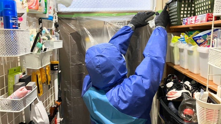 青い防護服を装着した自社スタッフが扉にマスカーテープを貼っている様子