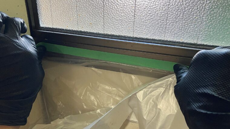 黒いグローブを装着し扉の上部にマスカーテープを貼っている様子